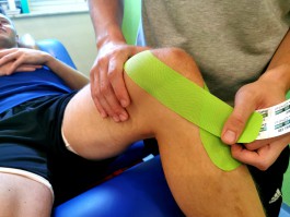 Kinesio-Tape wird auf ein Knie angebracht 